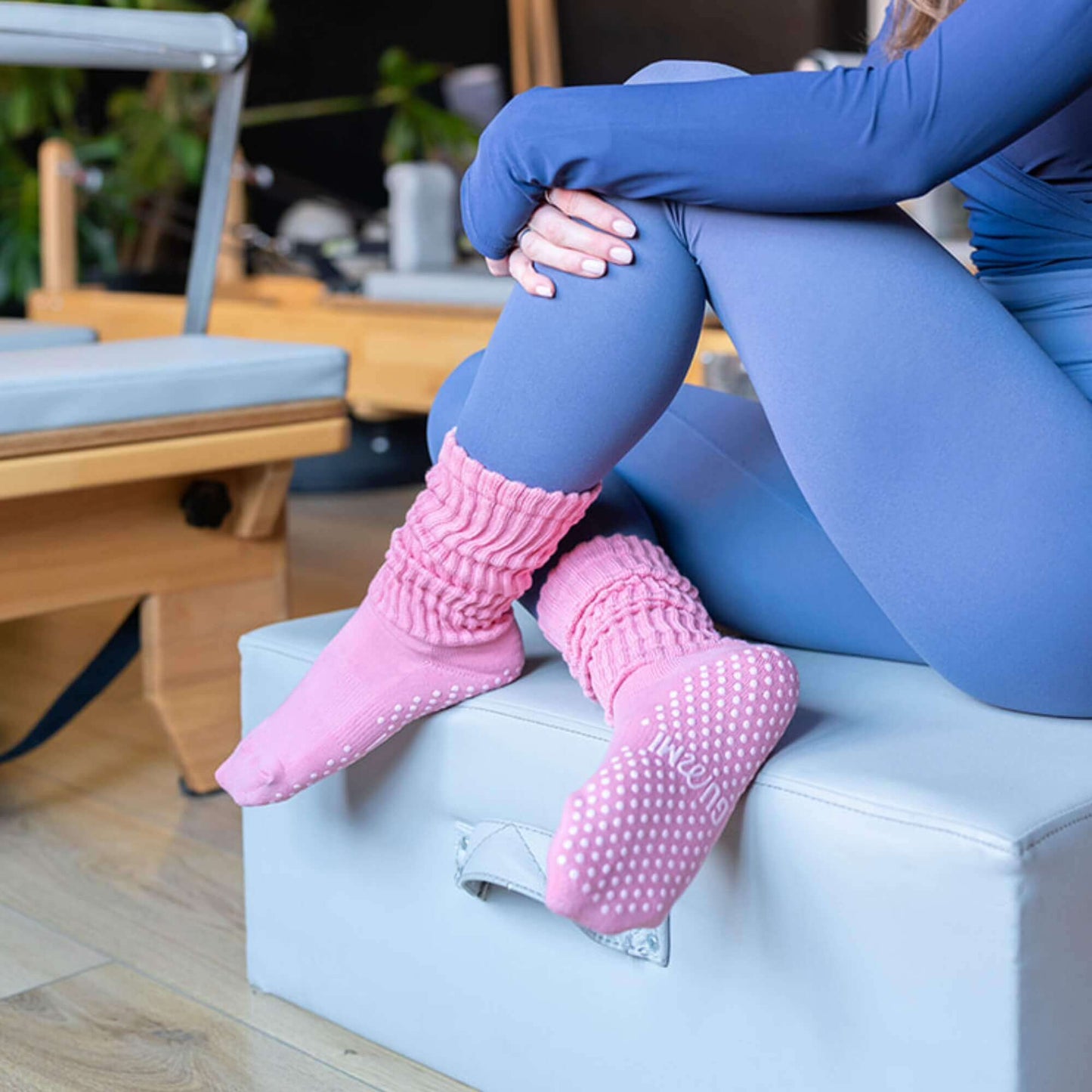 Model wearing Strawberry Fluff pink slouch grip socks seated on a Pilates reformer, showing relaxed scrunched fit and non-slip sole, suitable for Pilates, reformer, yoga and barre.