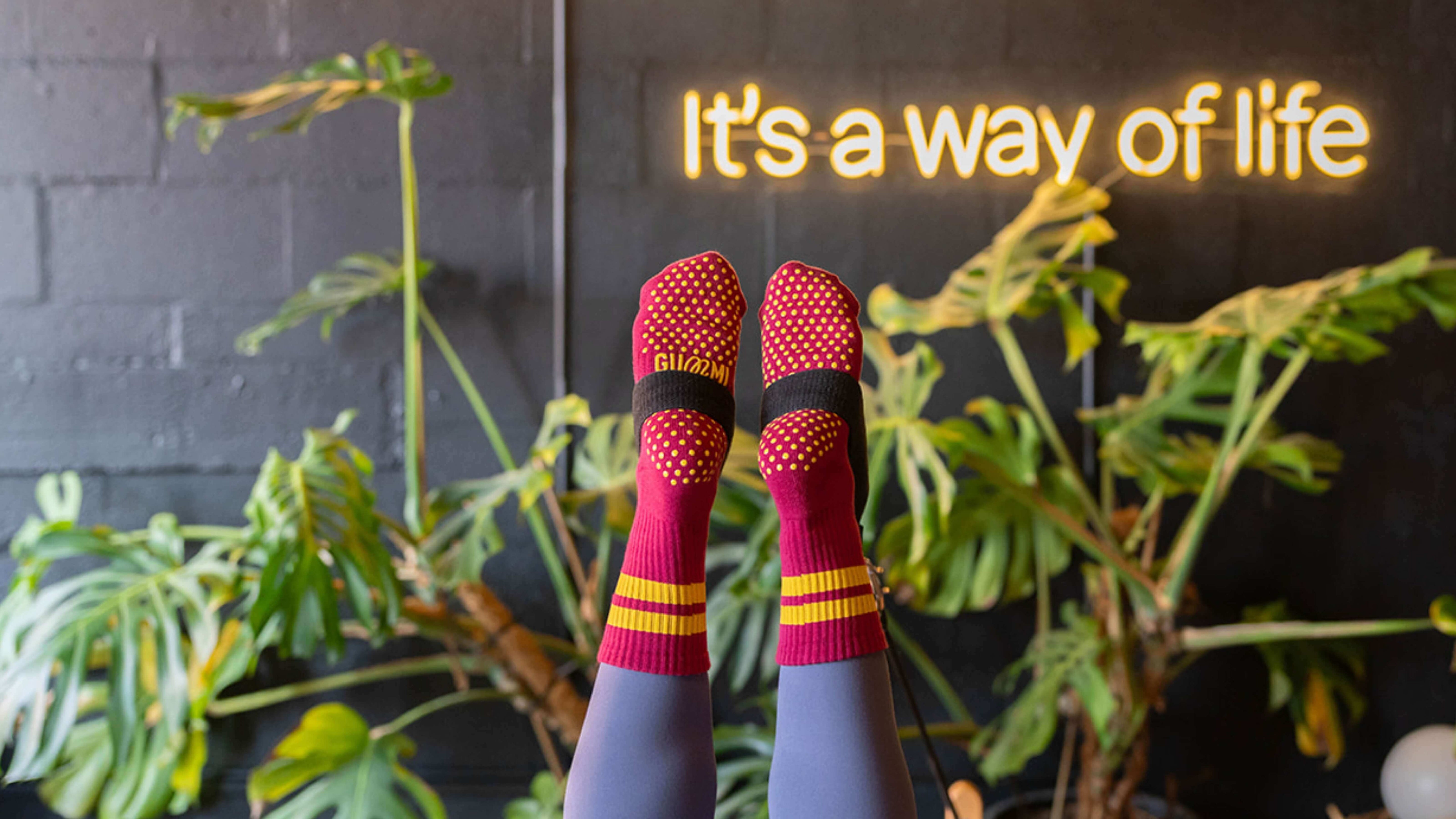 Person wearing red and yellow pilates socks infront of a sign that reads "It's a way of life".
