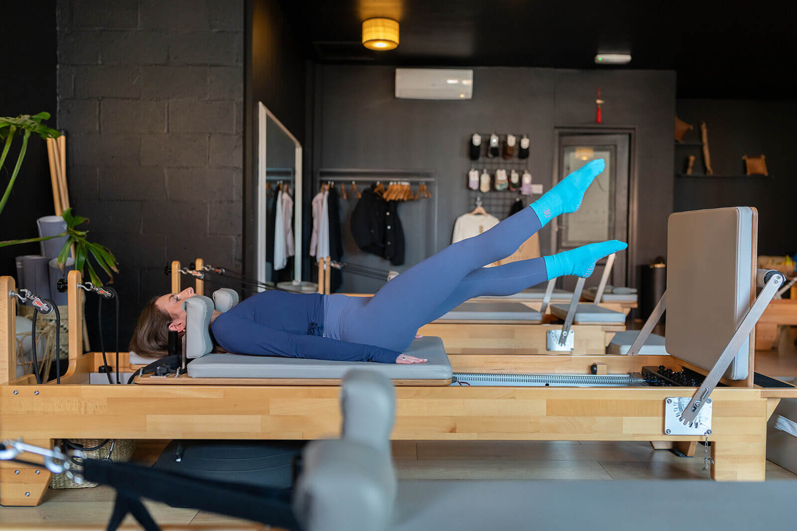 Person using a Pilates reformer machine in a studio setting, wearing blue pilates socks.