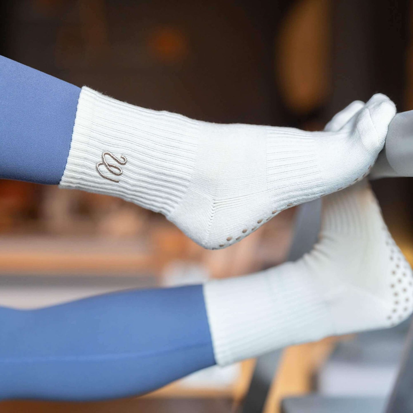 Gummi Socks white crew-length grip socks with ribbed cuff and cushioned sole, worn during a Pilates reformer exercise in a studio, suitable for reformer, yoga and barre.