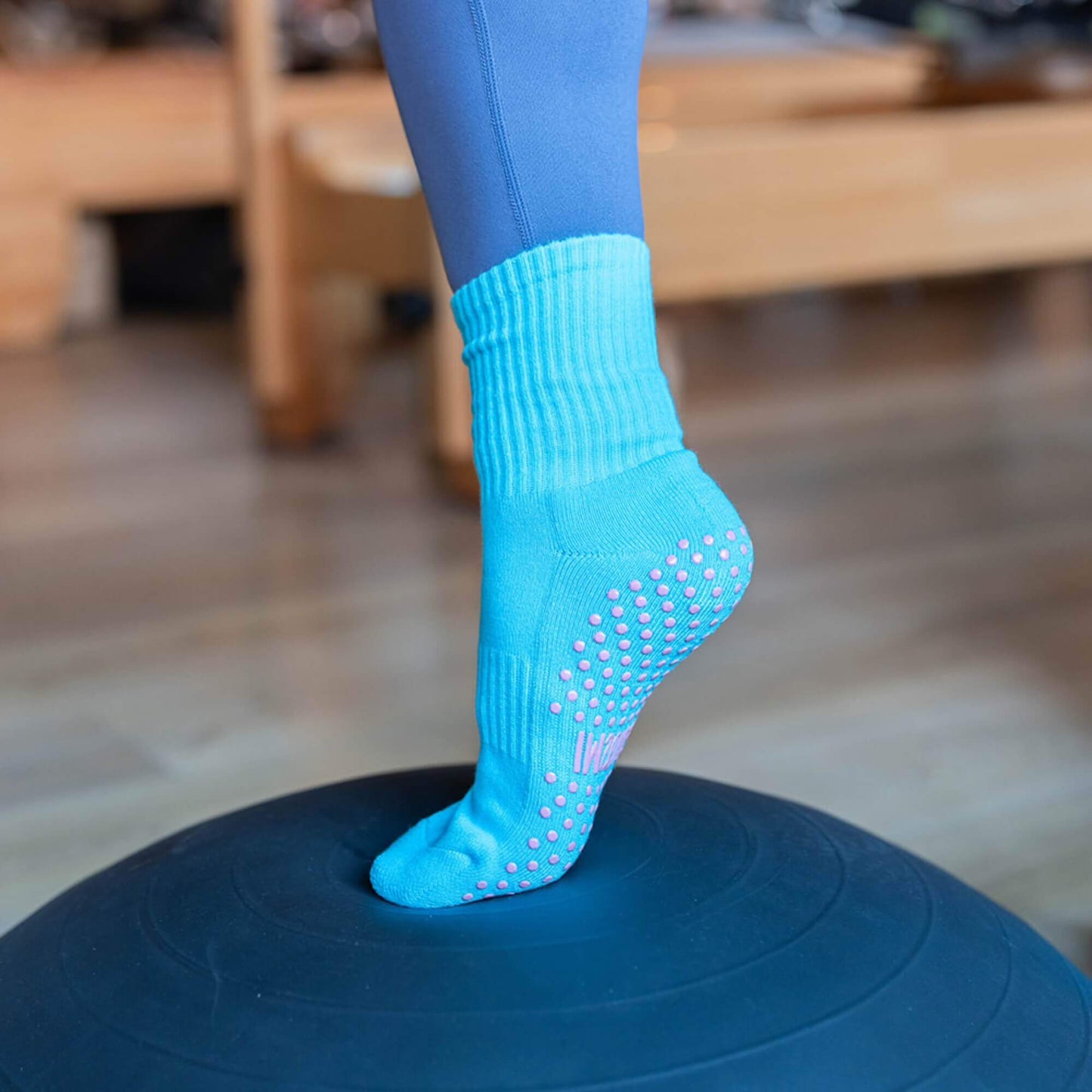 Gummi Socks Soft Serve Crew grip socks in blue, worn on foot balancing on Pilates equipment, showing snug crew fit, cushioned sole and non-slip grip for Pilates, reformer, yoga and barre.
