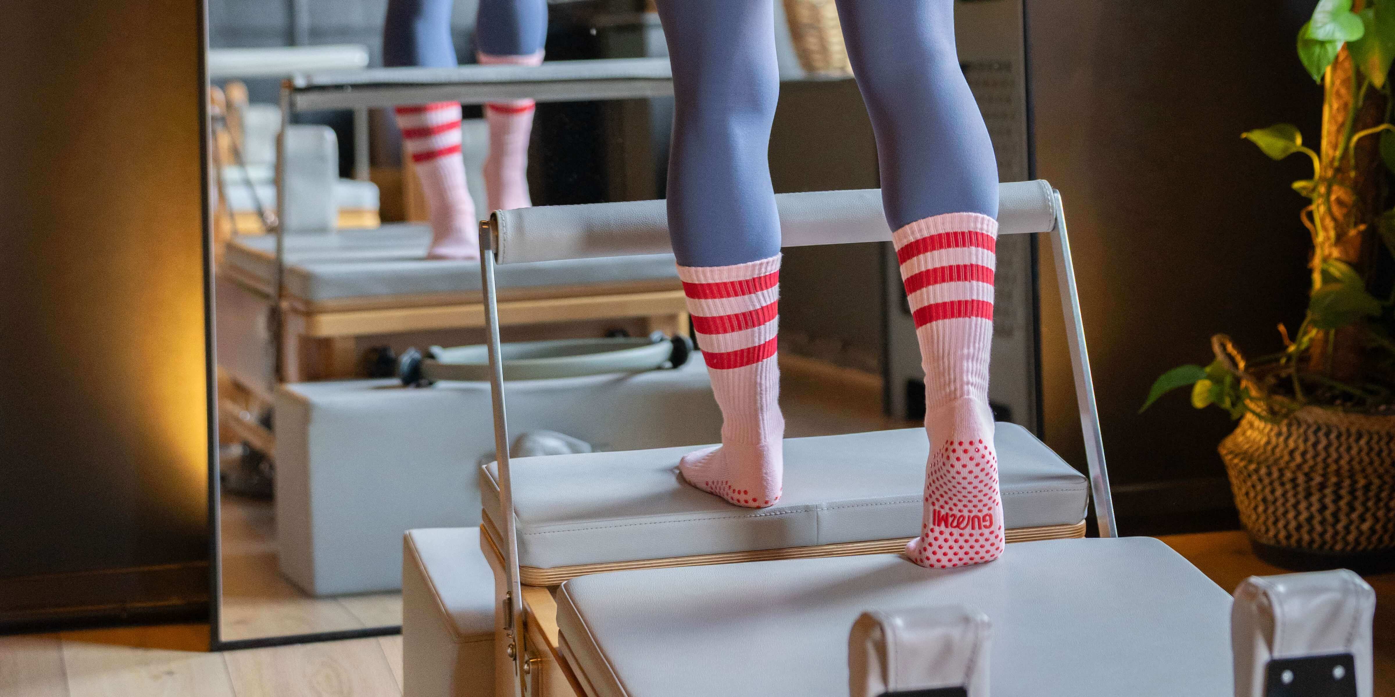 Person wearing striped grip socks standing on a reformer pilates bed.