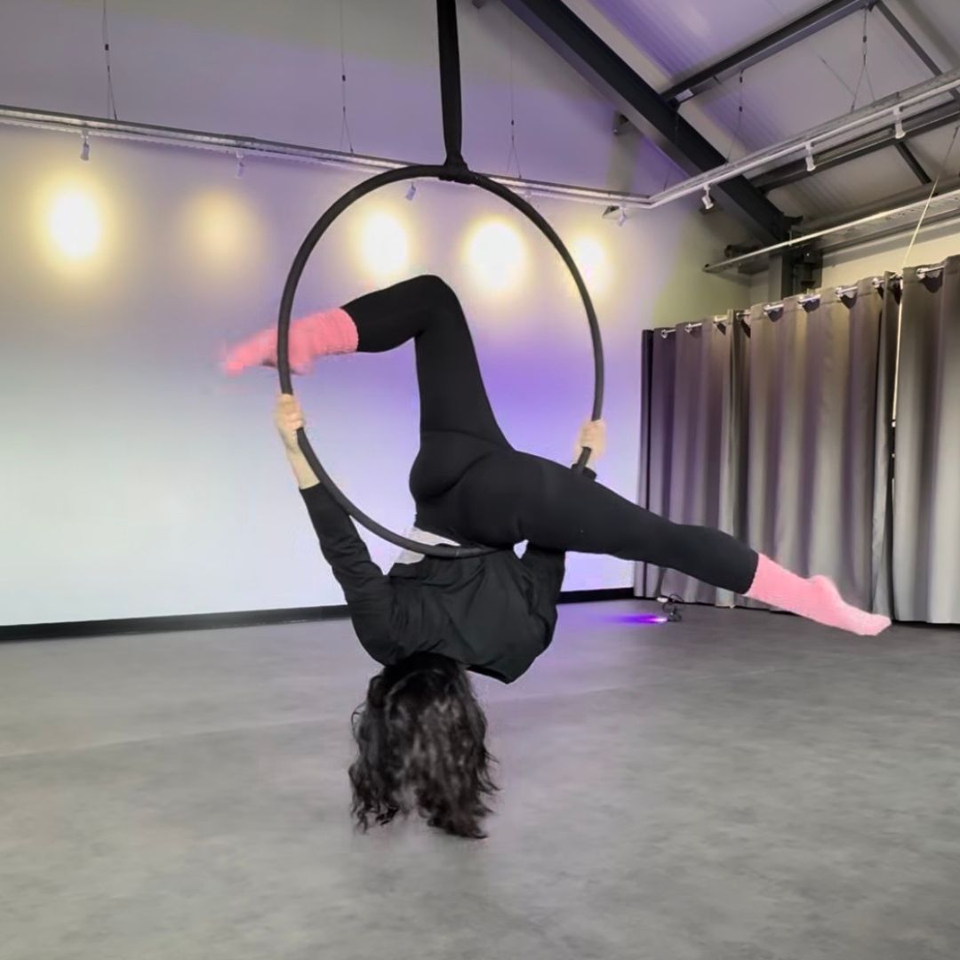 Person performing aerial hoop acrobatics in a studio setting