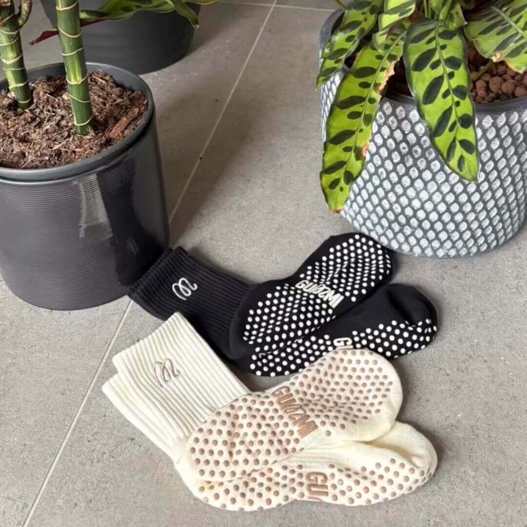 Black and cream pairs of GUMMI grip socks next to plants